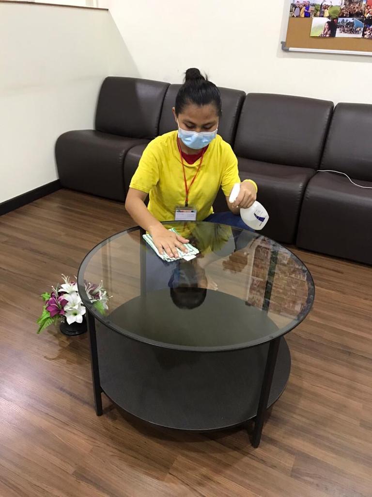Angel Cleaning team member wiping a glass table, with hands and spray bottle visible